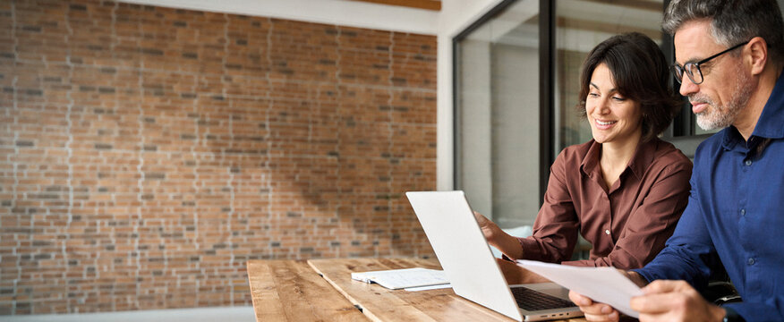 Two busy professionals man and woman business executives checking document working together on laptop in office. Financial advisor manager lawyer and investor discussing corporate project at meeting.