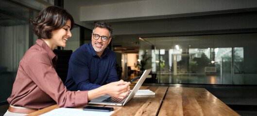 Business team two happy busy executives working together using laptop in office. Young business...