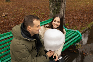 Young couple eating cotton candy on park bench 