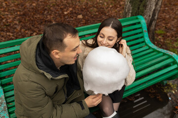 Young couple eating cotton candy on park bench 