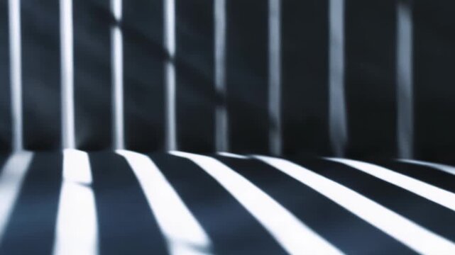 Strong light beams creating a dynamic abstract pattern of parallel stripes and shadows across a dark floor and wall, symbolizing themes of hope and confinement
