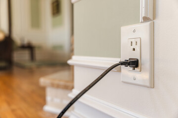 Power cable plugged into American electrical outlet in modern home interior, close view of wall...