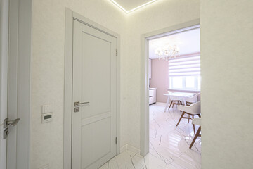 A bright hallway with white door, textured wallpaper, marble-like flooring leads to a dining area...