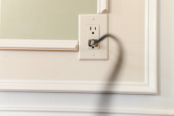 Blurred power cable plugged into American wall outlet on decorative interior wall with white...