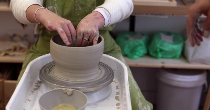 Experienced male potter teaching a female student how to shape a clay vase on a potter's wheel, showing her the traditional techniques for creating handmade ceramic art in a workshop