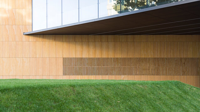 Modern building facade with natural stone cladding and green grass lawn in foreground