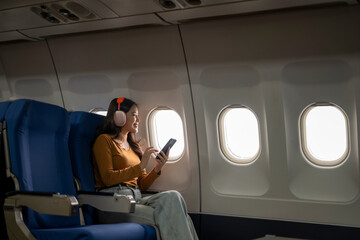 Young woman listening music and using smartphone on airplane flight