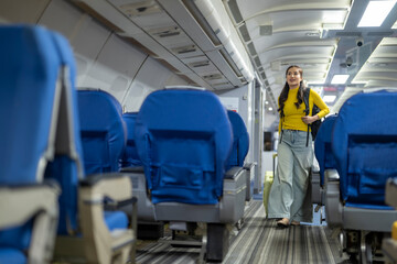 Young woman walking down airplane aisle pulling carry-on luggage