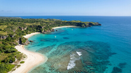 Obraz premium Aerial view of pristine beach with turquoise water and lush green coastline. The serene beach features white sand and clear ocean with gentle waves.