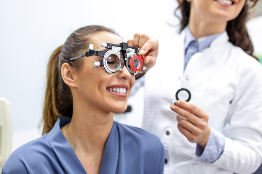 Eye exam with trial frame and lenses for vision correction. Smiling patient undergoing optometry test with professional ophthalmologist to determine glasses prescription.