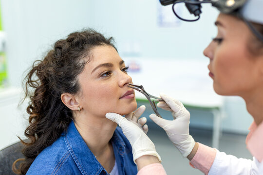 ENT doctor specialist performing nasal examination on patient. Professional otolaryngologist using medical speculum for nose diagnostic and respiratory health screening in modern clinic.