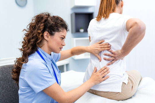 A female healthcare professional examines the lumbar spine and lower back of a patient sitting on a treatment bed, focusing on pain relief, spinal health, and orthopedic injury rehabilitation.