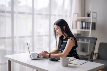 Focused woman typing on laptop at modern office desk