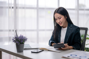 Asian businesswoman calculating financial data and using calculator in office