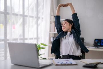 Businesswoman stretching at office desk after work on laptop computer