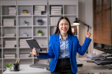 Excited businesswoman celebrating success with tablet in office