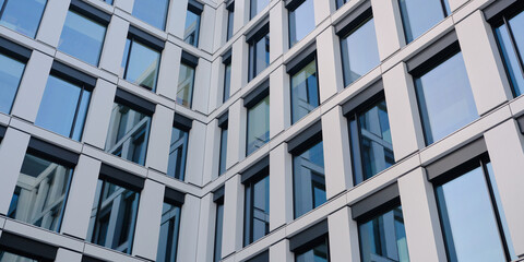 Modern office building facade with glass windows and metal panels forming a clean geometric pattern, contemporary architecture background for corporate and design use.