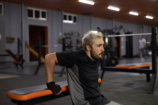 Focused man performing triceps dips on gym bench