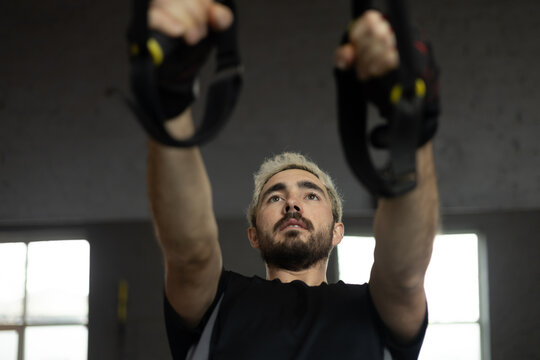 Focused man exercising with suspension straps in gym