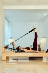 Woman Doing Pilates On Reformer Machine With Straps In Modern Home Studio