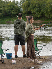 Young man and woman enjoying fishing together on riverbank, casting lines and waiting for a catch...
