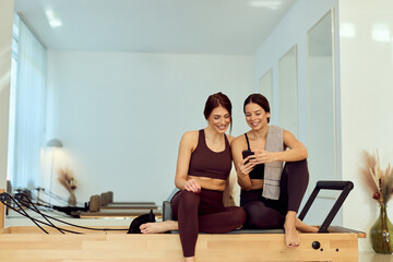 Two Friends Relax After Pilates Session On Wood Reformer In Bright Gym Studio