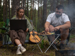 Freelancers enjoying camping trip in nature, combining work and leisure, with man preparing...