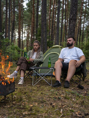 Young couple relaxing by a cozy bonfire, sipping beer and enjoying each other's company during a...