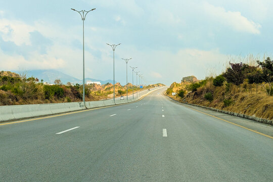 A beautiful winding road going through a patch of green trees on each side.Kashmir Road near Chattar Park, Punjab, Pakistan (01-23-2026) car and trafice View of Ring Road, Ring Road interexchange Isla