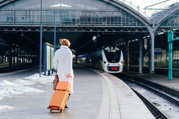 Caucasian redhead woman walking with suitcase toward arriving train © Iryna