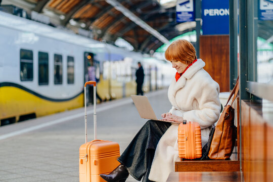 Successful middle aged caucasian redhead woman working on laptop at train station platform