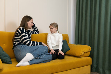 Obraz premium Mother and daughter seriously talking on a yellow couch at home, discussing problems and communicating about important family issues, focusing on parenting and child development