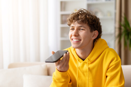 Teen guy using smartphone at home, smiling while speaking on voice call, dressed in yellow hoodie, relaxed on sofa, enjoying technology, connection, and casual lifestyle indoors