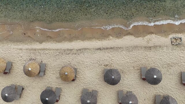Top down aerial drone footage of a sandy beach with sun umbrellas, loungers and gentle sea waves in Halkidiki, Greece. Mediterranean coastline, summer vacation, seaside resort and travel tourism conce