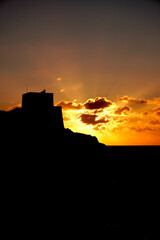 Obraz premium Striking silhouette of ancient fortress ruins on hilltop against fiery orange sunset sky, dramatic Malta landscape at dusk