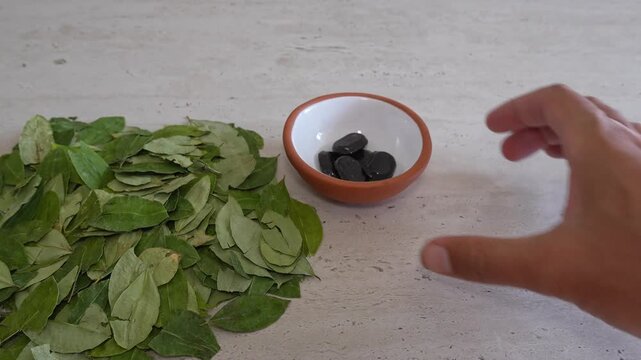 Person placing a small bowl of coca candies next to a pile of dried coca leaves. This traditional andean remedy helps with altitude sickness