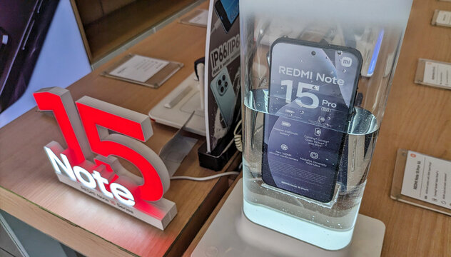 A display case for the Redmi Note 15 Pro smartphone at an electronics store is displayed in a transparent container filled with water to demonstrate its waterproof feature. 