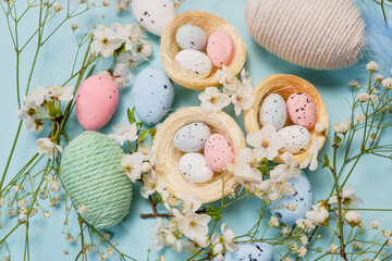 Flat lay of Easter eggs, decorative nests, and blue feathers on pastel blue background, greeting...