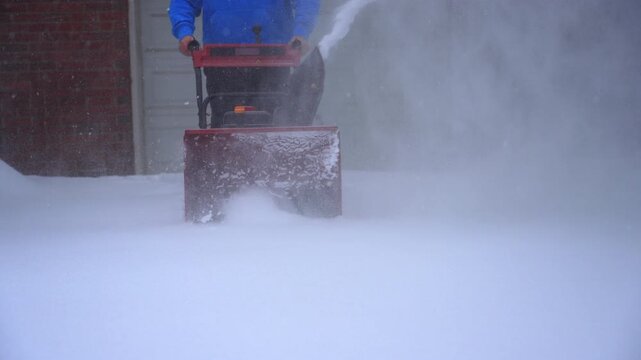 Man using snowblower to clear driveway.
