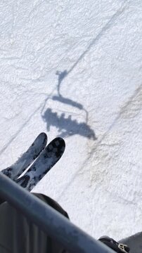 Vertical shot Skis positioned on a ski lift chair with their shadow visible on the snow, highlighting a winter sports scene at a ski resort. Side view of a skier on the ski lift