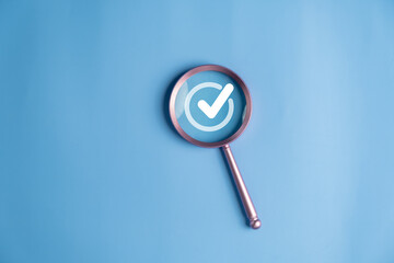 Magnifying glass highlighting a check mark icon on blue background, representing verification, approval, quality control, inspection, confirmation, trust, and successful validation concept