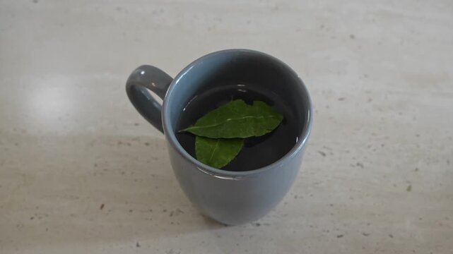 Persons hand placing coca leaves into a ceramic cup filled with steaming water. This ancient andean brew is known to be an effective natural treatment for altitude sickness