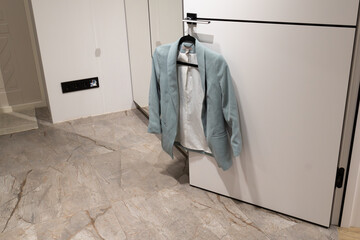 A light jacket hangs on a door in a room with white walls and light tiles. The setting shows a clean and organized space