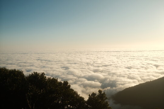 Dreamlike Ocean of Clouds Under Golden Sunset Sky Viewed from Mountain Edge. Horizontal Photo with Copy Space.