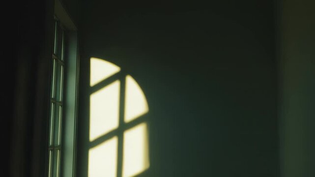 Warm sunlight streams through a window, creating a striking grid pattern of light and shadow on a muted wall and floor, evoking feelings of peace and solitude