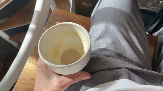 POV hand holding a small cup with leftover coffee at the cafe