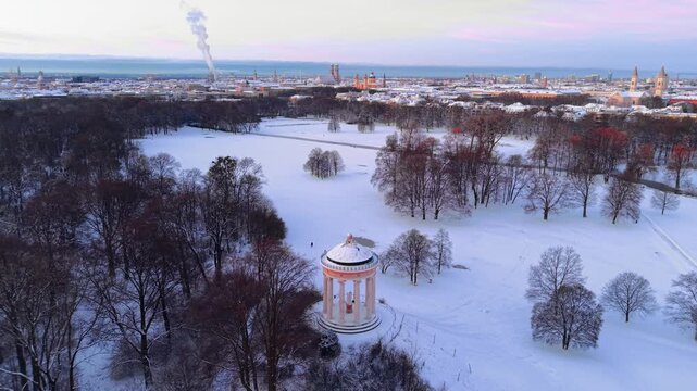 Golden hour over snowy Munich, Germany. Winter morning showing Monopteros viewpoint and scenic vista of the old town architectural heritage under a clear sunrise sky. Luftaufnahme Englischen Garten