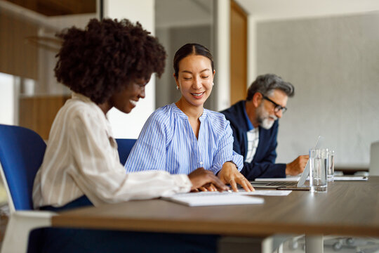 Female professionals discussing business data and strategies in modern office while male colleague working in the background