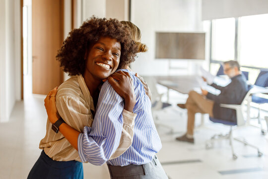 Happy mid adult businesswoman comforting and motivating female colleague with warm embrace in modern office