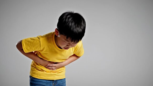 little asian boy suffering from strong stomach ache, holding belly with hands. unhappy kid feeling abdominal pain, indigestion or poisoning. healthcare concept.